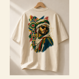 T-shirt oversize écru suspendu à un cintre en bois, présenté de dos. Il porte un grand visuel coloré représentant un homme au turban et aux lunettes, accompagné de motifs géométriques.